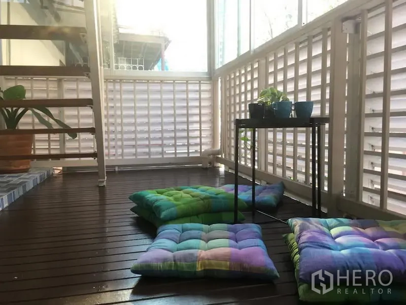 Townhouse for rent in Bang Rak, Bangkok - Covered balcony with wooden decking, lattice walls, floor cushions, small plant table and stairs.