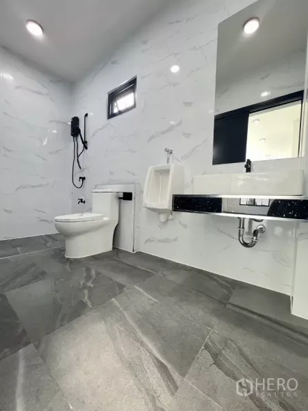 Warehouse for sale in Lam Luk Ka, Pathum Thani - Clean modern restroom with toilet, urinal, vanity and marble-look wall tiles.