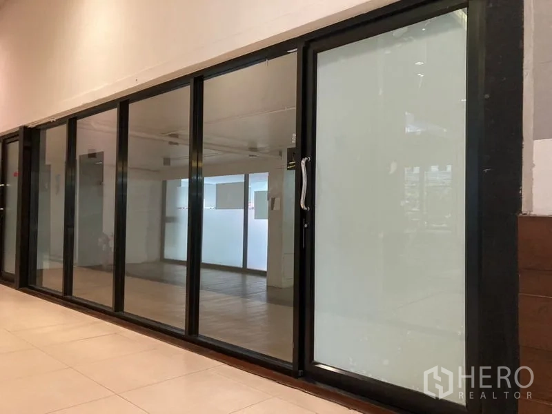 Retail Space for rent in Khlong Toei, Bangkok - Glass-front retail unit with black aluminum sliding doors along an indoor corridor in Ekkamai, Bangkok.