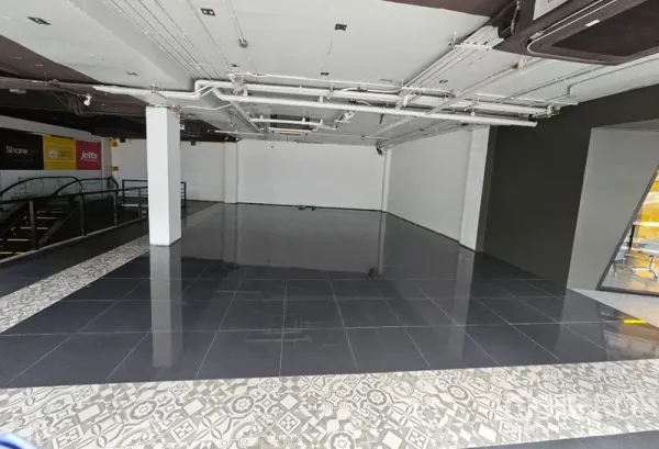 Retail Space for rent in Bang Rak, Bangkok - Open-plan retail unit with glossy black tiles, white walls, exposed ceiling services, and escalator access inside a mall.
