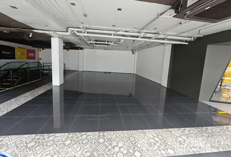 Retail Space for rent in Bang Rak, Bangkok - Open-plan retail unit with glossy black tiles, white walls, exposed ceiling services, and escalator access inside a mall.