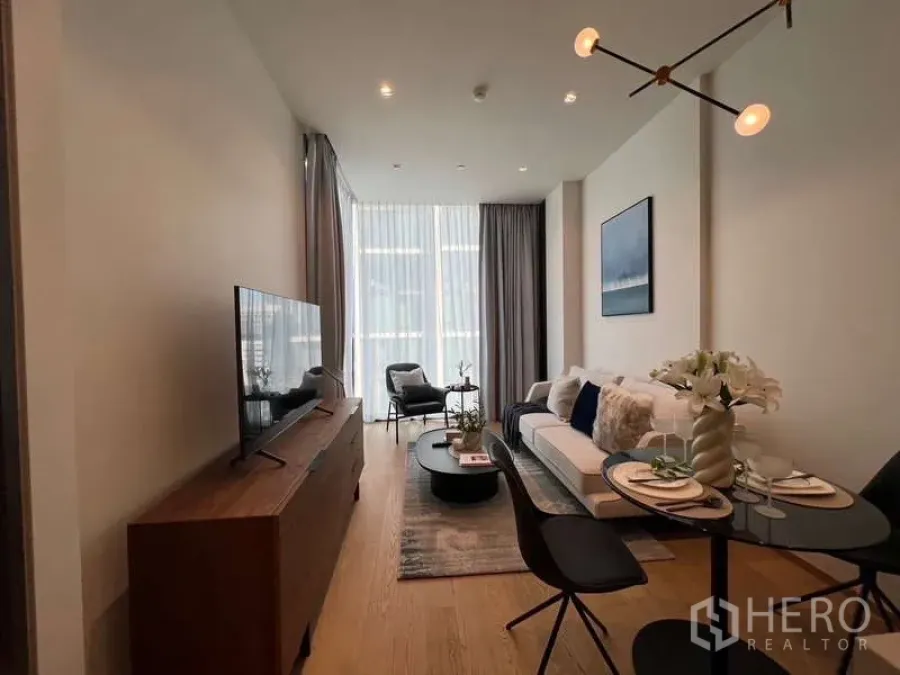 Condominium for rent in Pathum Wan, Bangkok - Open-plan living room with designer pendant light, coffee table and high windows bringing in natural light.