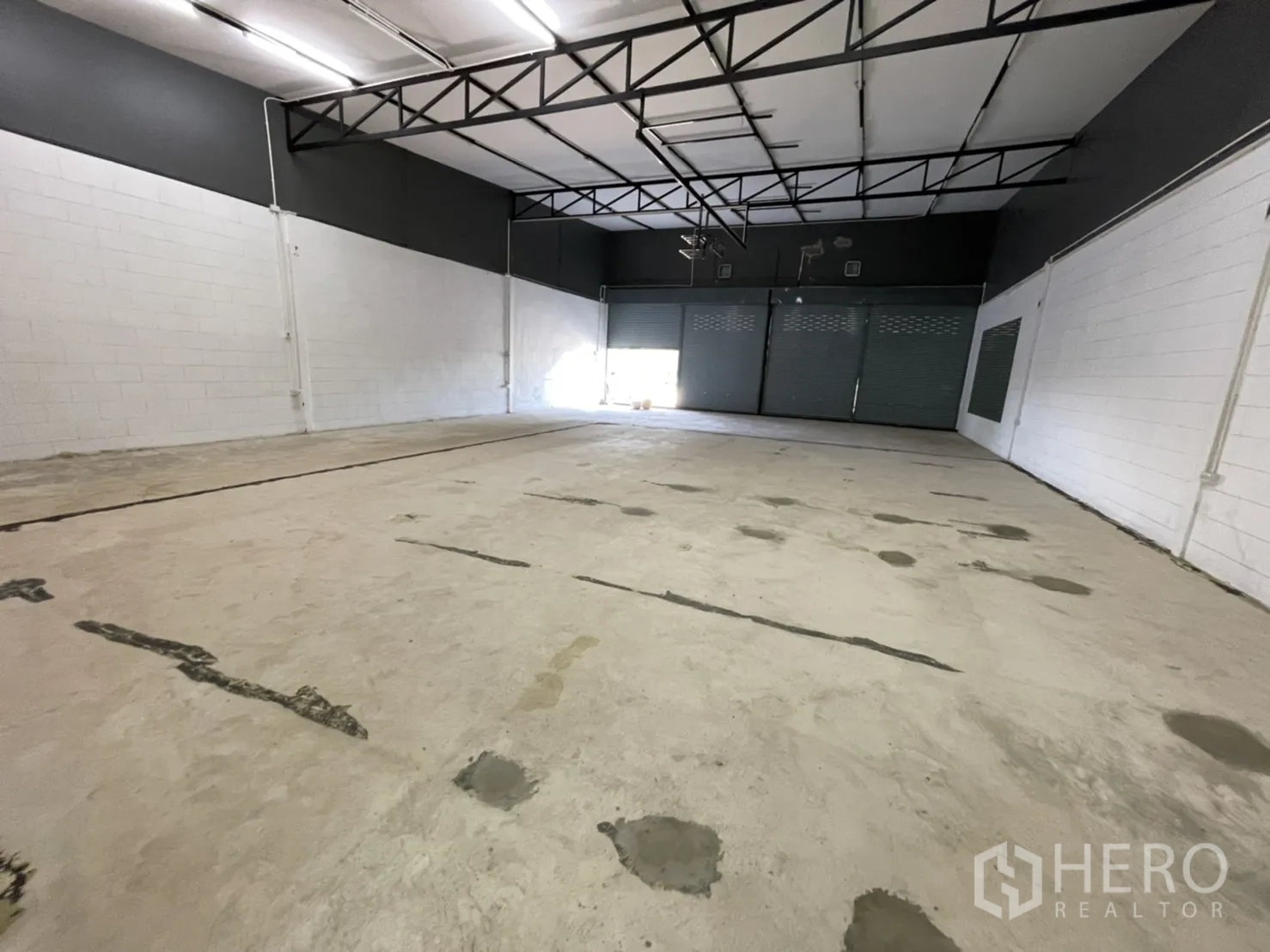 货栈 出租在Lam Luk Ka, Pathum Thani - 宽阔仓库跨间，光滑混凝土地面与涂装砖墙，前方为卷帘门。