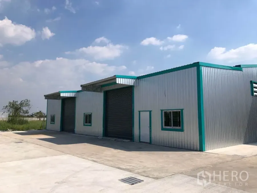Warehouse for rent in Pak Kret, Nonthaburi - Modern metal-clad warehouse with three roller shutter doors and a wide concrete yard in Pak Kret.