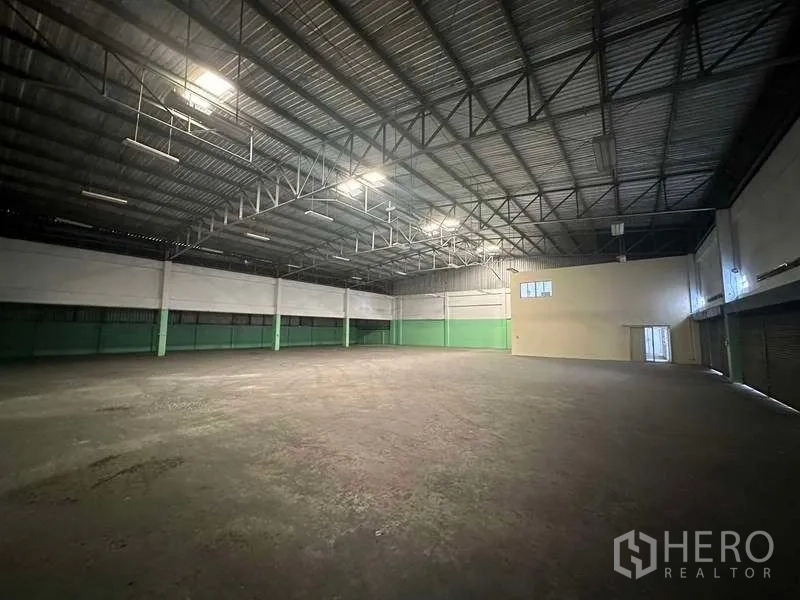 โรงงาน ให้เช่าในNonthaburi - โถงผลิตโล่ง เพดานทรัสเหล็ก ผนังล่างสีเขียว พร้อมประตูขนถ่ายด้านข้าง.