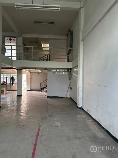 Shophouse for rent in Khlong Toei, Bangkok - Mezzanine level with railings and stair access above an open retail floor with white walls and concrete tiles.