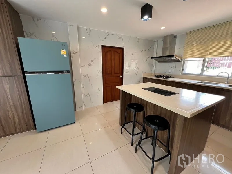 Detached House for sale in Mueang Pathum Thani, Pathum Thani - Contemporary kitchen with island cooktop, stools and a matte blue refrigerator.