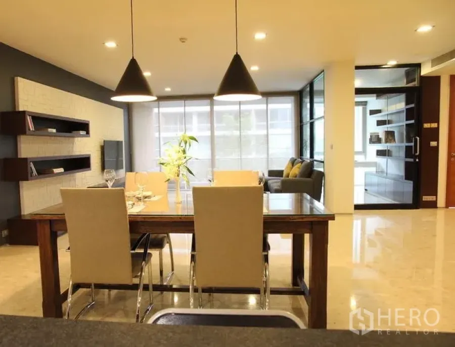 Condominium for rent in Khlong Toei, Bangkok - Dining area flowing to a bright living room with floor-to-ceiling windows and built-in shelving.