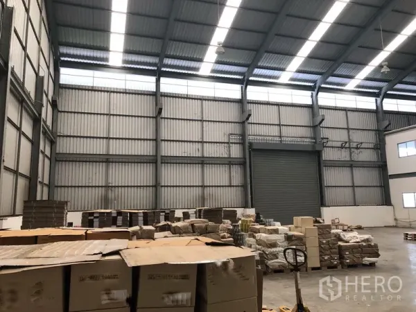 工厂 出租在Khlong Luang, Pathum Thani - 带天窗与钢梁的仓库大厅，堆放托盘，配有大型卷帘门。