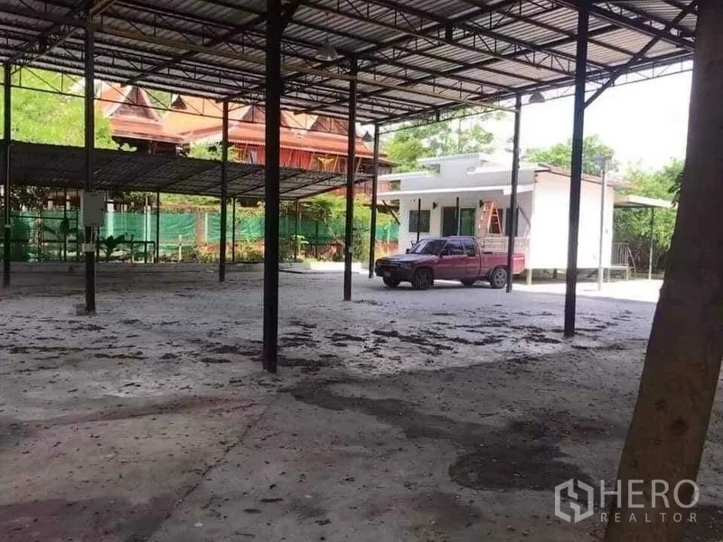Warehouse for rent or sale in Khlong Sam Wa, Bangkok - Wide sheltered yard with steel roof structure and a compact office building.