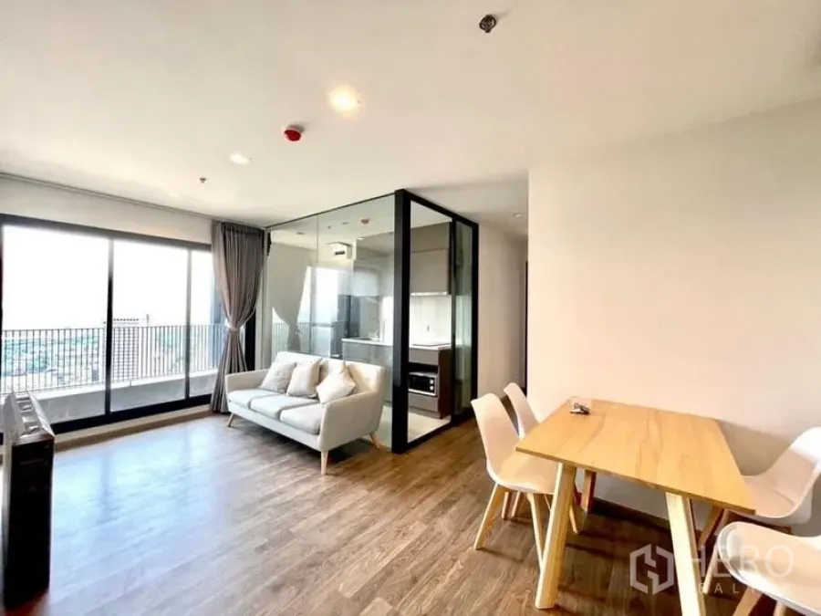 Condominium for rent in Chatuchak, Bangkok - Open-plan living room with wood floors, sofa, dining table and balcony access.
