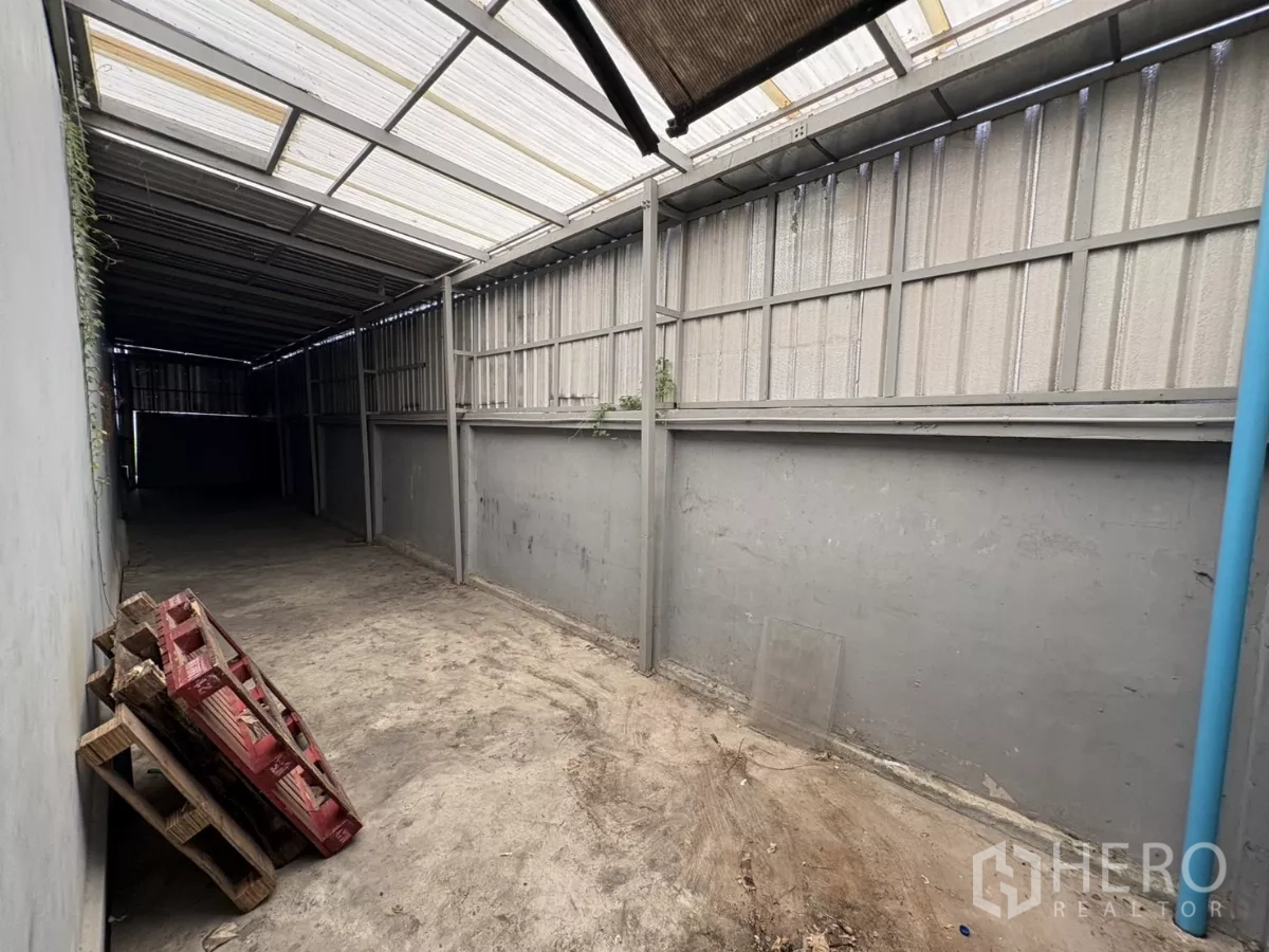 Warehouse for rent in Bang Phli, Samut Prakan - Covered side yard with metal roof and concrete floor for storage or loading.