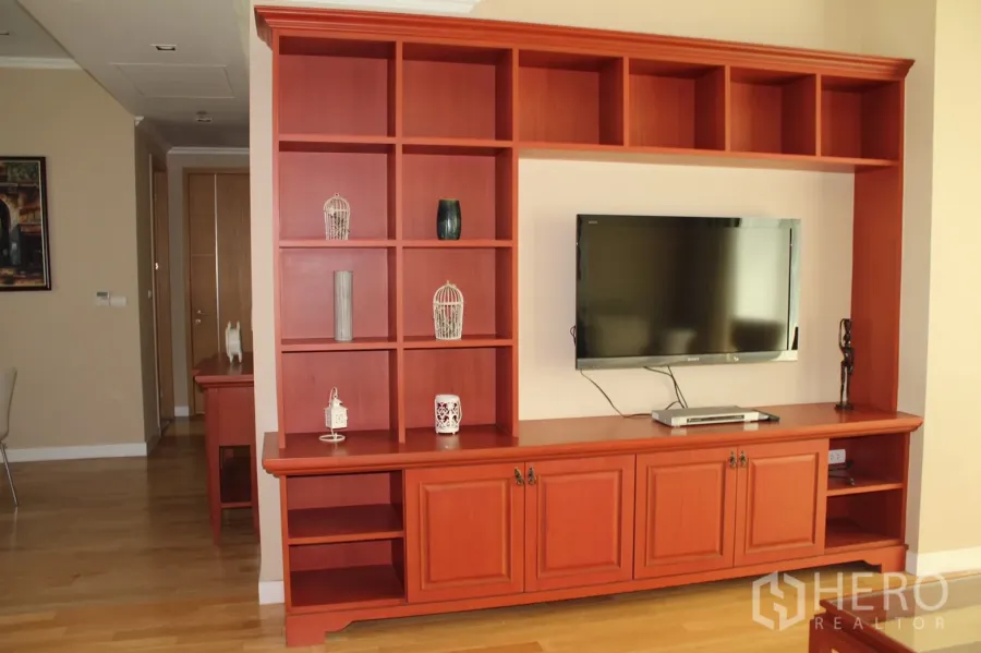 Condominium for rent in Khlong Toei, Bangkok - Living room with custom red wood entertainment wall, shelving and mounted TV on hardwood floors.