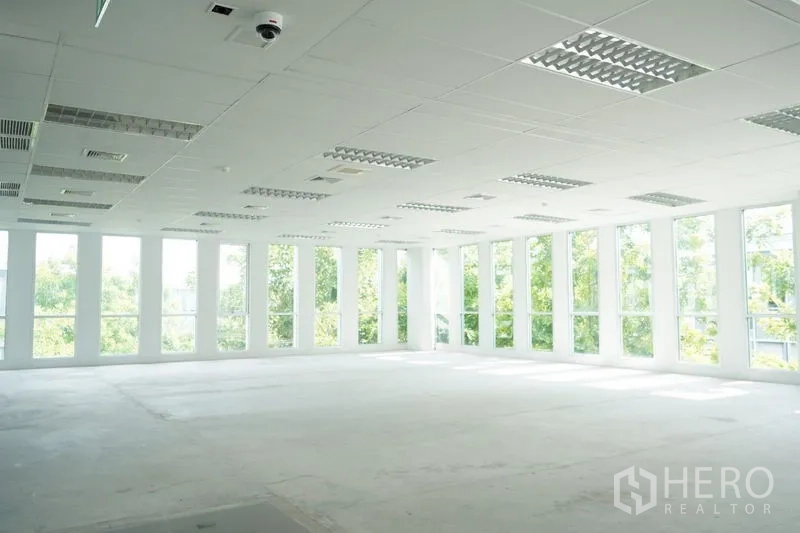 Office Space for rent in Bang Na, Bangkok - Bright empty office interior with floor-to-ceiling windows, white grid ceiling, lighting fixtures and greenery views near BTS Bearing.