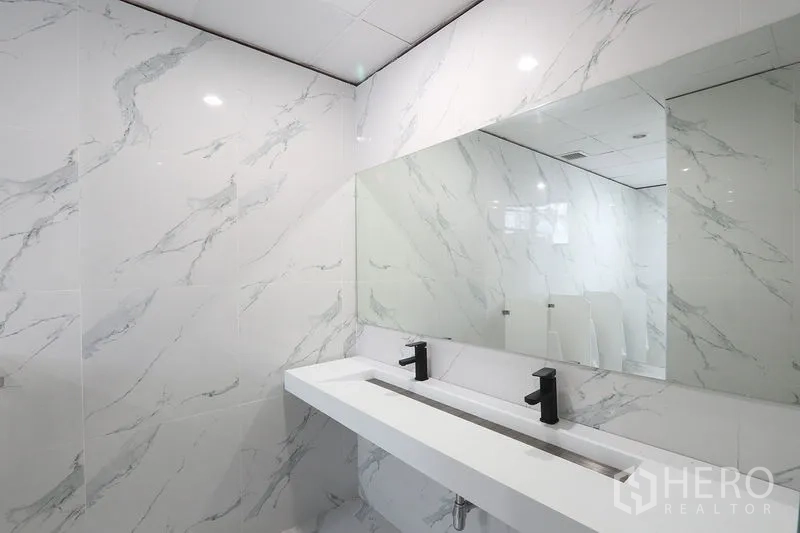 Office Space for rent in Bang Na, Bangkok - Renovated restroom with marble‑look tiles, long trough sink and matte black faucets.