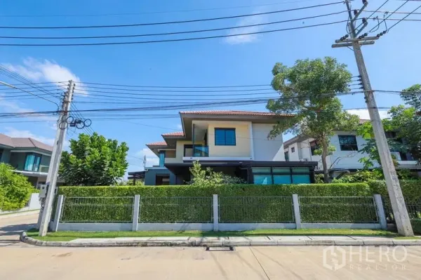Detached House for rent or sale in Lam Luk Ka, Pathum Thani - Corner two-storey detached house with tall hedge fence and gated frontage in Lam Luk Ka.