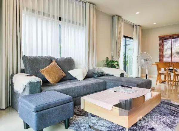 Detached House for sale in Lam Luk Ka, Pathum Thani - Bright living room with large grey sectional sofa, sheer curtains and a wooden coffee table.