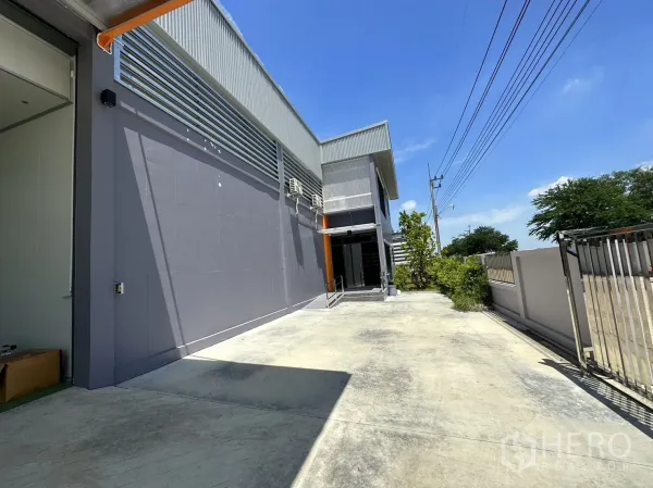Factory for sale in Lam Luk Ka, Pathum Thani - Modern factory facade along a private driveway with gated entry.