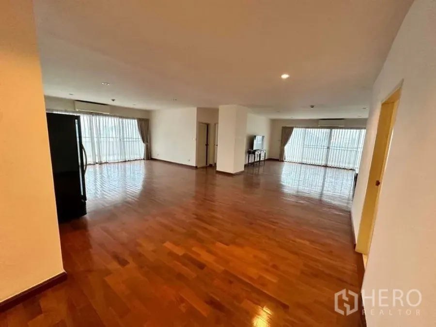 Condominium for rent in Bangkok - Wide living area with floor-to-ceiling windows on two sides and shiny wooden floors.