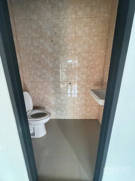 Warehouse for rent in Lam Luk Ka, Pathum Thani - Tiled restroom with a toilet and wall-mounted sink inside the facility.