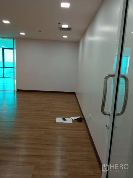 Office Space for rent in Huai Khwang, Bangkok - Office corridor with glass door and stainless handles, recessed ceiling lights, and wood floors opening to an open-plan area.