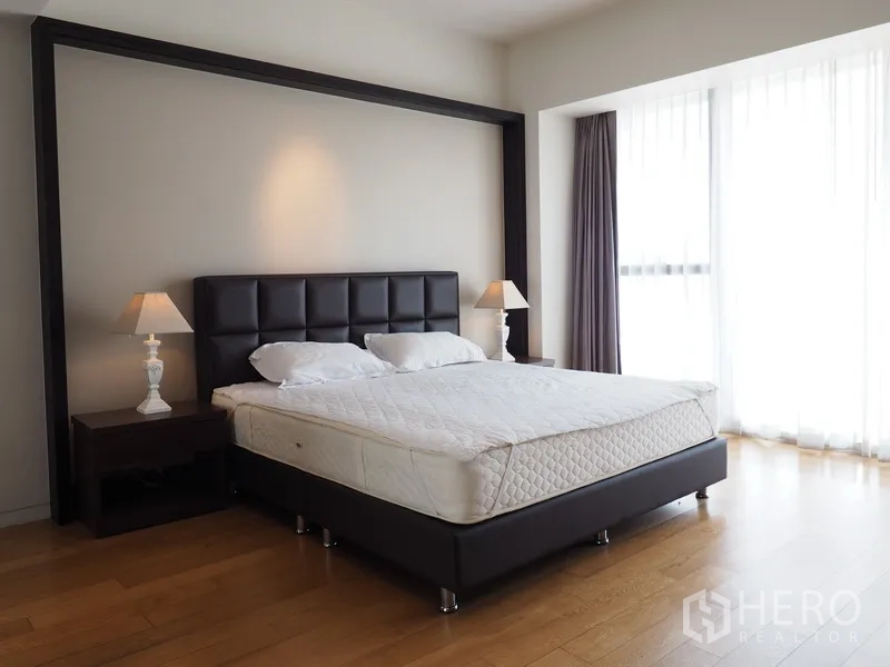 Condominium for rent in Sathon, Bangkok - Bright master bedroom with wood floors, bedside lamps and full-height windows with sheer curtains.