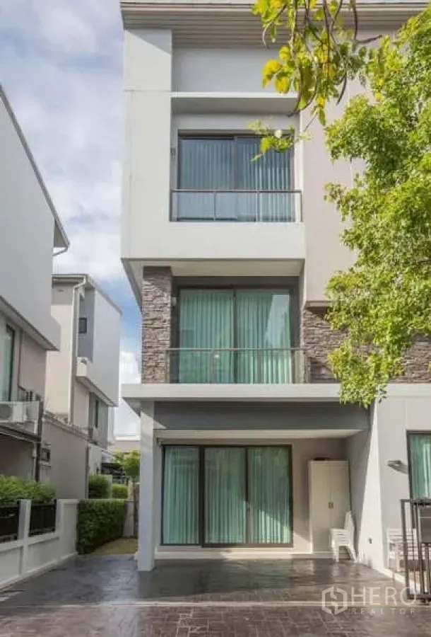 Detached House for rent or sale in Lat Phrao, Bangkok - Three-storey modern detached house facade with large windows and a balcony in Lat Phrao, Bangkok.