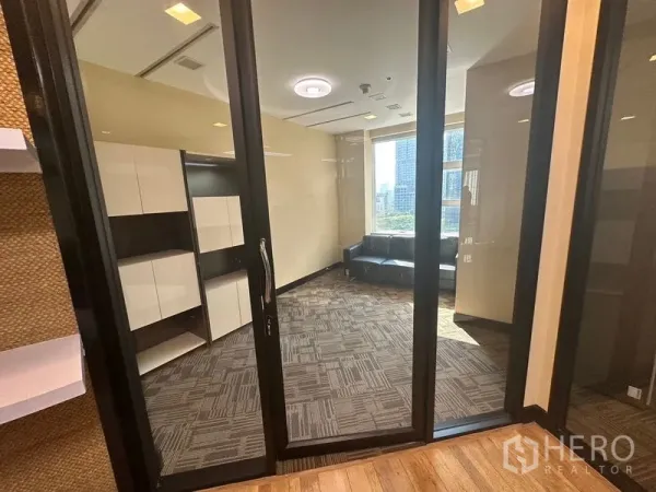 Office Space for rent - Private office behind glass partitions with carpet tiles, built-in cabinets and a sofa by the window with city views.