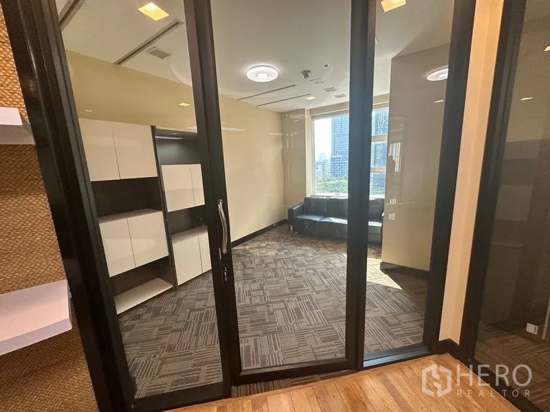 Office Space for rent - Private office behind glass partitions with carpet tiles, built-in cabinets and a sofa by the window with city views.