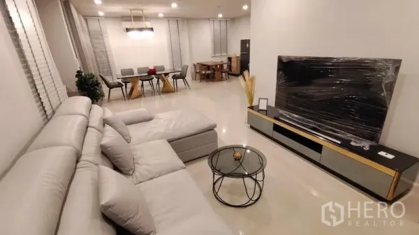 Detached House for rent in Prawet, Bangkok - Open-plan living room with large L-shaped grey sofa, TV console and glass coffee table.