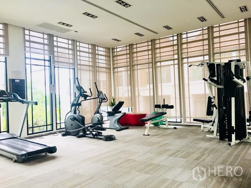 Townhouse for rent in Prawet, Bangkok - A fitness room with treadmills, bikes and weight machines beside tall windows.