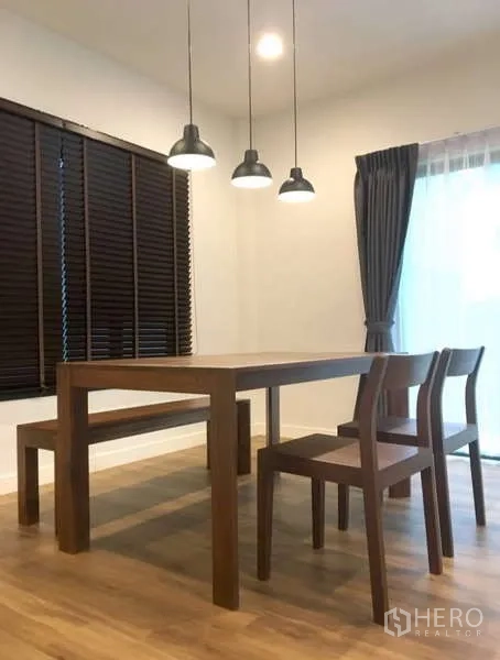 Detached House for rent in Bang Kapi, Bangkok - Minimal dining set with bench and chairs under pendant lights by the curtains.