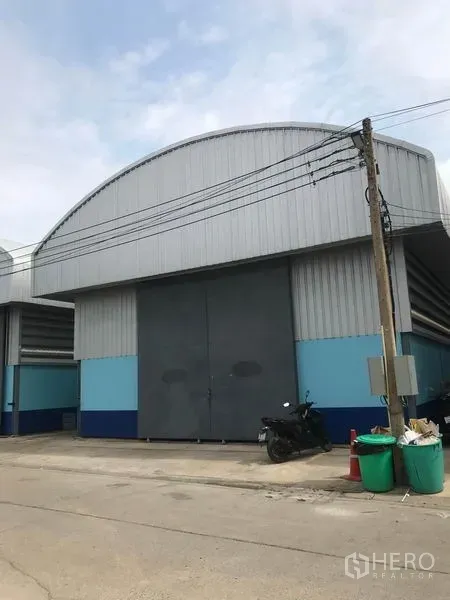 Warehouse for rent in Khlong Luang, Pathum Thani - Front elevation of the warehouse with large steel double doors and ample driveway access.