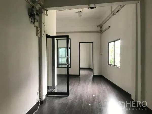 Shophouse for rent in Watthana, Bangkok - Open-plan floor with dark laminate, interior glass door and side window connecting multiple rooms.