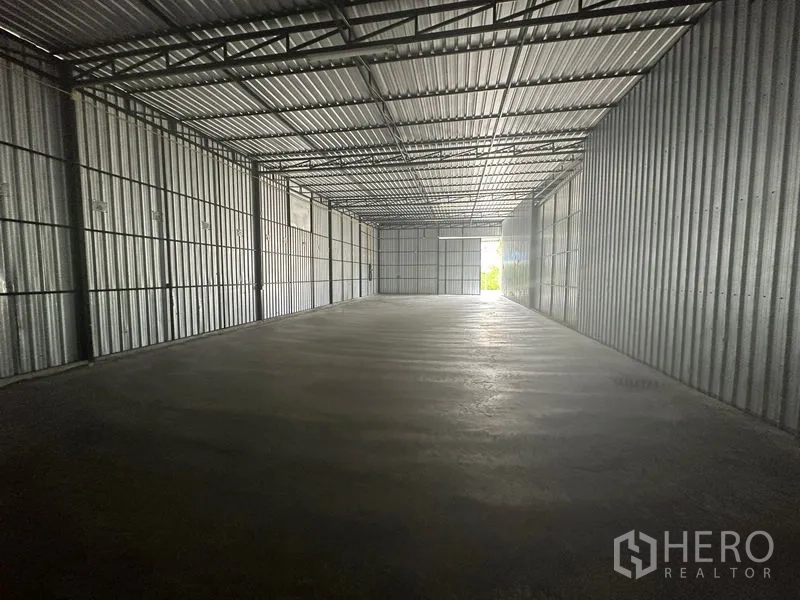 Warehouse for rent in Wang Thonglang, Bangkok - Long open-plan warehouse with corrugated metal walls, polished concrete floor, and natural light at the wide end door.