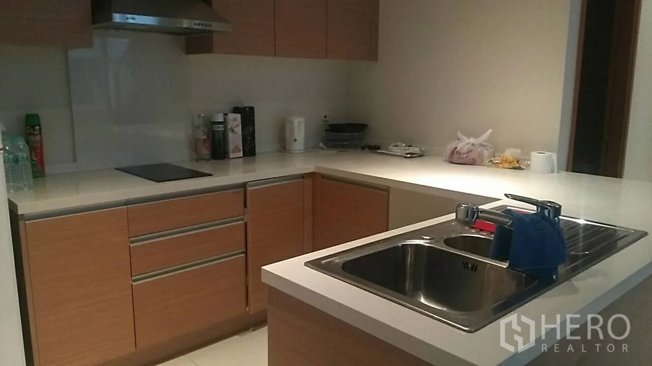 Condominium for sale in Khlong Toei, Bangkok - Modern L-shaped kitchen with wood cabinets, island sink, cooktop and range hood in a Bangkok condo.