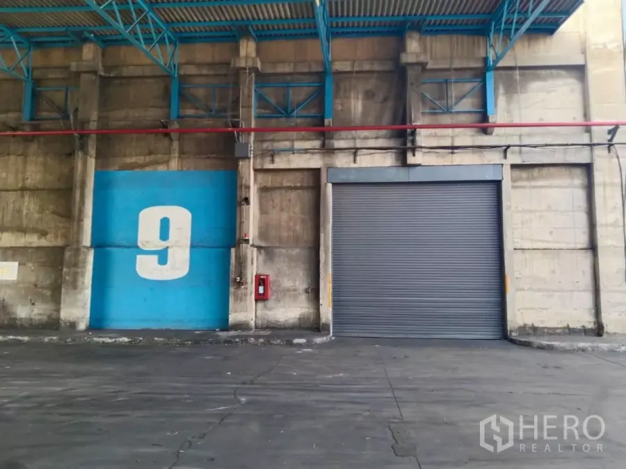 Factory for rent in Samut Prakan - Covered loading bay with large roller shutter door, bay number signage, and fire safety point.