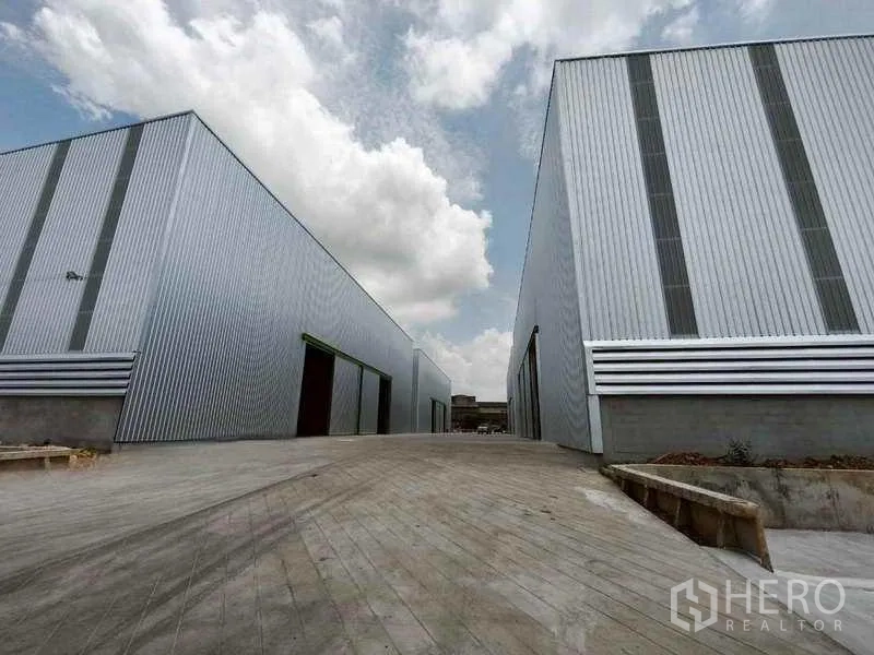 Warehouse for rent in Bang Phli, Samut Prakan - Modern metal-clad warehouse buildings with a wide concrete driveway in Bang Phli under open skies.