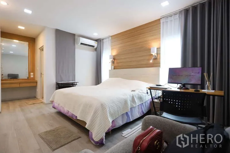 Detached House for rent or sale in Prawet, Bangkok - Master bedroom with wood accent wall, desk area, and large curtained windows.