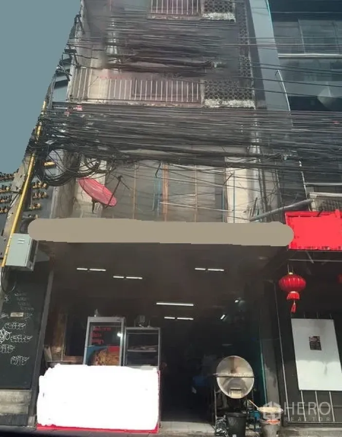 店屋 出售在Watthana, Bangkok - 曼谷Watthana区街边店屋外立面，店面敞开、玻璃展示与红色灯笼，门前上方有密集电缆。