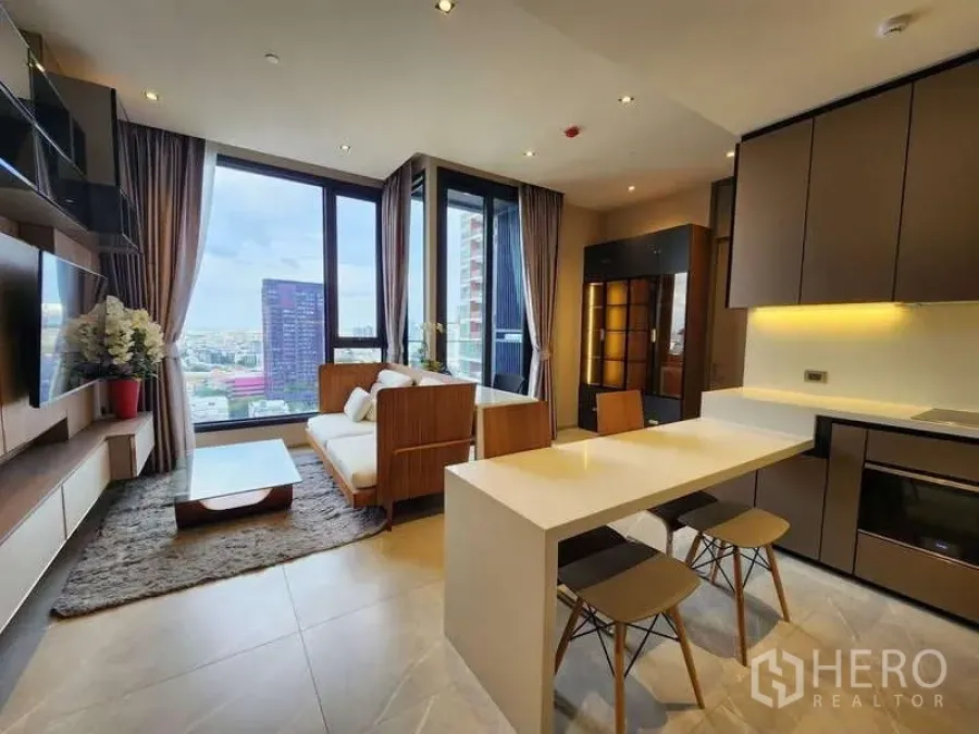Condominium for rent in Watthana, Bangkok - Open-plan living and kitchen with island seating and tall windows framing the skyline.