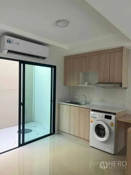 Townhouse for rent in Suan Luang, Bangkok - Kitchenette with sliding door to service area, air conditioner above and built-in cabinetry.