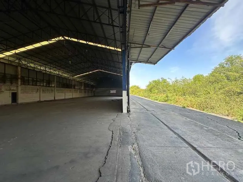 Warehouse for rent in Wang Noi, Phra Nakhon Si Ayutthaya - Partially open warehouse bay with covered platform and wide truck lane beside greenery.