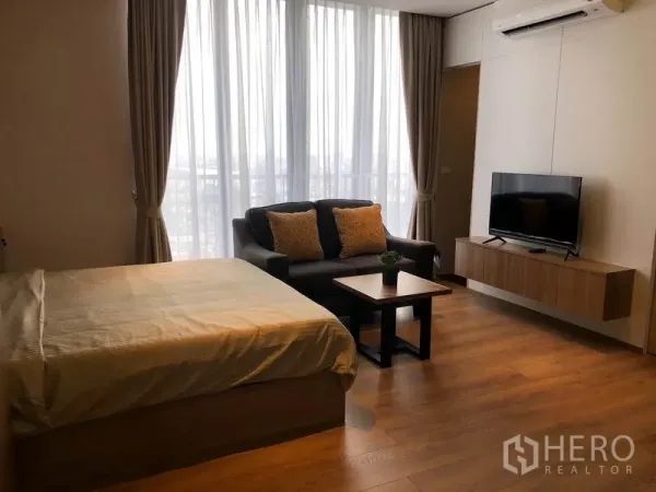 Condominium for rent in Khlong Toei, Bangkok - Bright room with bed, sofa, wall-mounted TV and full-height balcony windows.