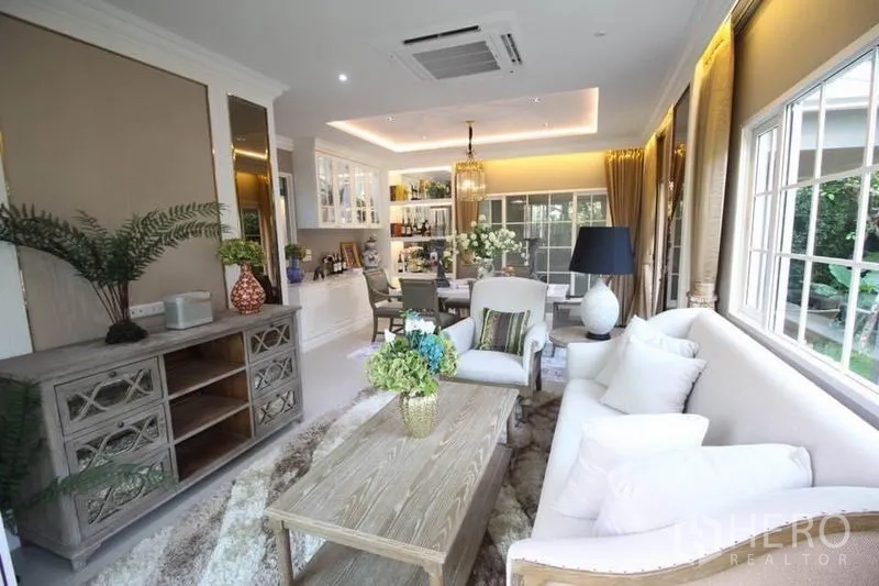 Detached House for rent or sale in Lat Phrao, Bangkok - Bright open-plan living and dining room with large windows, cove lighting, white sofa and built-in cabinetry.