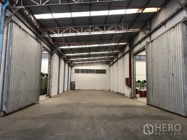 Warehouse for rent in Bang Bua Thong, Nonthaburi - Empty warehouse bay with high steel truss roof and large sliding metal doors.