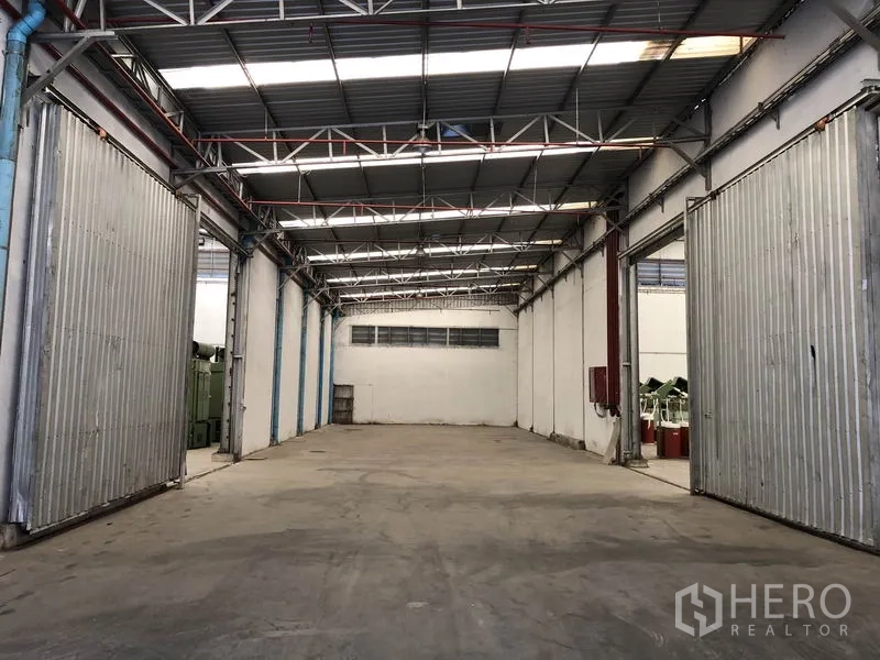 Warehouse for rent in Bang Bua Thong, Nonthaburi - Empty warehouse bay with high steel truss roof and large sliding metal doors.