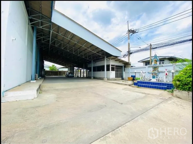 Factory for rent in Sam Phran, Nakhon Pathom - Open courtyard under a long roof canopy beside the office wing and a small shrine.