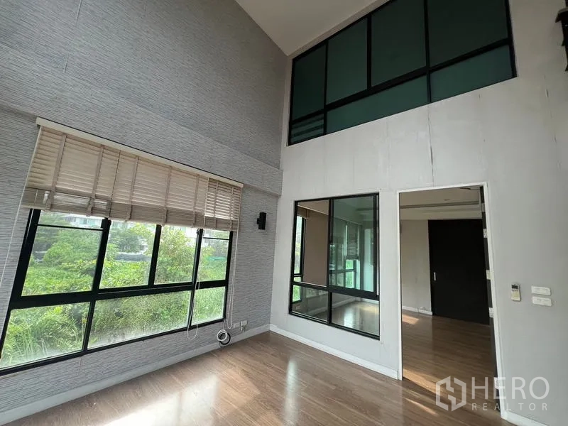 Townhouse for rent or sale in Khlong Toei, Bangkok - Double-height room with large windows and mezzanine-style glass panels facing greenery.