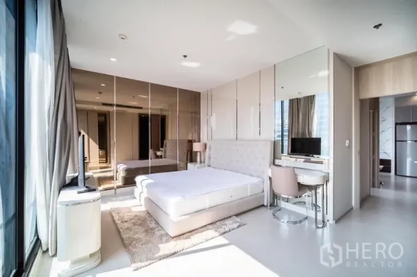 Condominium for rent in Pathum Wan, Bangkok - Spacious bedroom with tufted headboard, vanity desk, glossy wardrobes and large window.